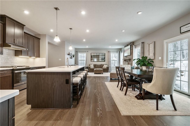 kitchen with decorative light fixtures, dark hardwood / wood-style floors, an island with sink, stainless steel gas range oven, and dark brown cabinetry