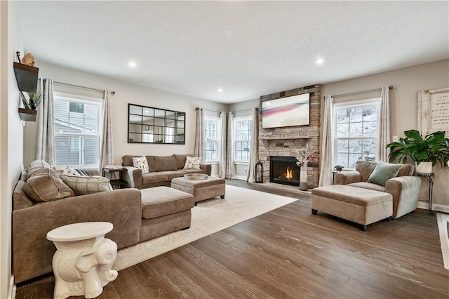 living room with wood-type flooring, a wealth of natural light, and a stone fireplace