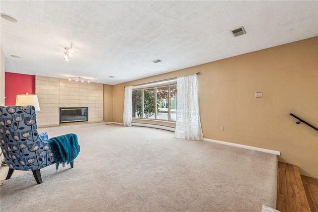 unfurnished room with track lighting, a baseboard radiator, carpet, and a tiled fireplace