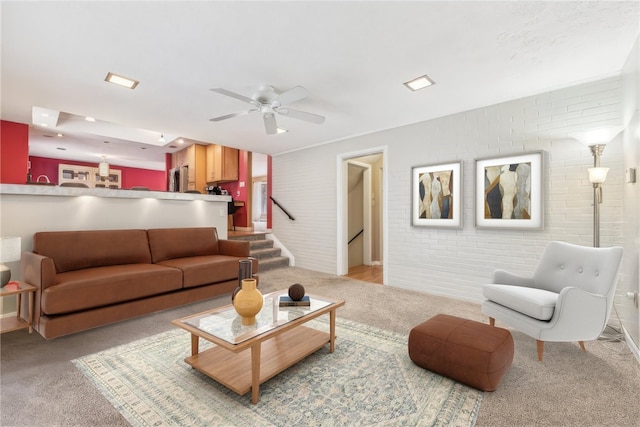 carpeted living room with ceiling fan and brick wall