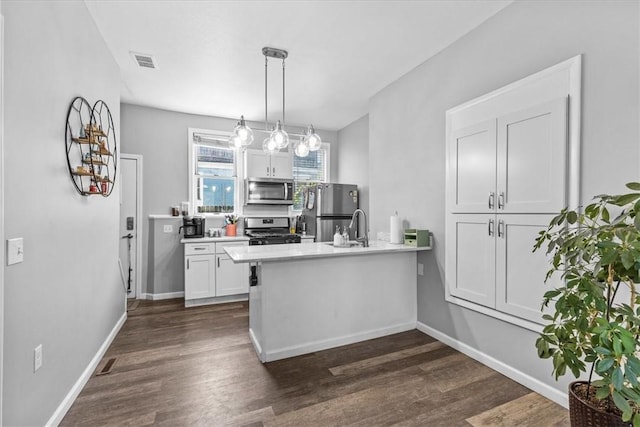 kitchen with stainless steel appliances, white cabinets, kitchen peninsula, hanging light fixtures, and dark hardwood / wood-style floors