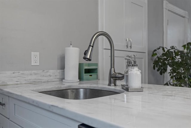 interior details featuring light stone countertops, white cabinets, and sink