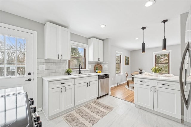 kitchen with stainless steel appliances, white cabinetry, hanging light fixtures, and sink