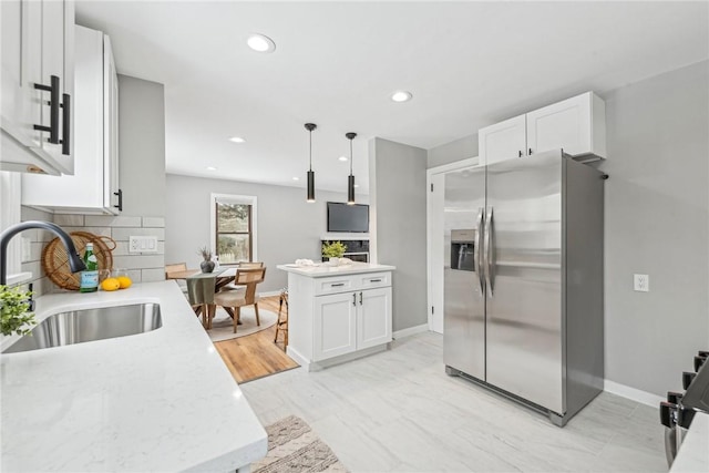 kitchen featuring hanging light fixtures, stainless steel fridge with ice dispenser, backsplash, white cabinets, and sink