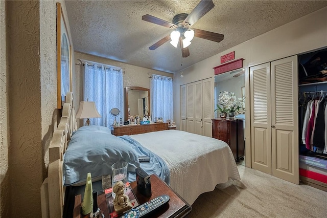 carpeted bedroom with ceiling fan, multiple closets, a textured wall, and a textured ceiling