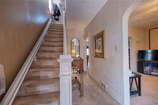 staircase with arched walkways, baseboards, carpet floors, and visible vents