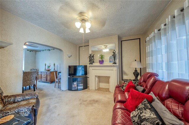 living room featuring ceiling fan, a textured wall, carpet floors, arched walkways, and a textured ceiling