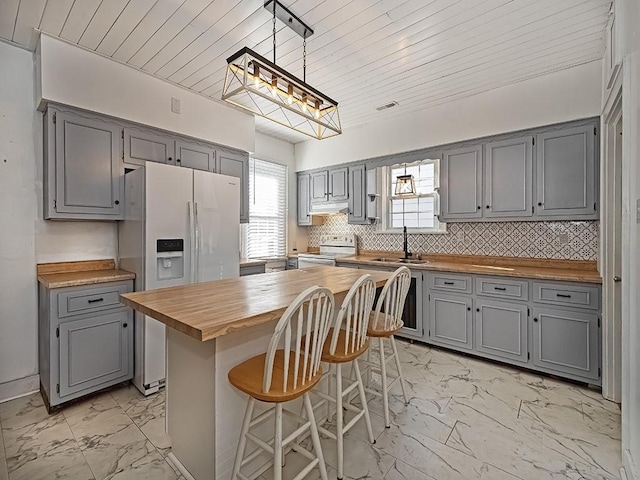 kitchen featuring sink, a center island, white appliances, decorative backsplash, and wooden counters