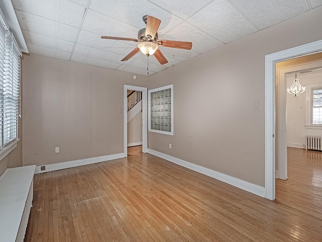 empty room with ceiling fan with notable chandelier, light wood-type flooring, and radiator heating unit