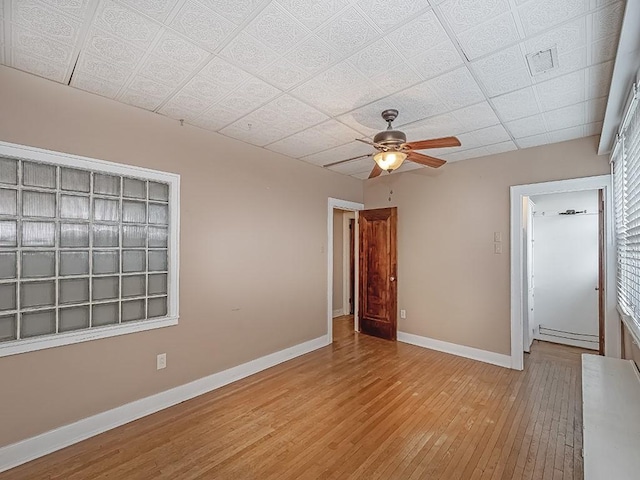 unfurnished room featuring a drop ceiling, a baseboard radiator, light wood-type flooring, and ceiling fan