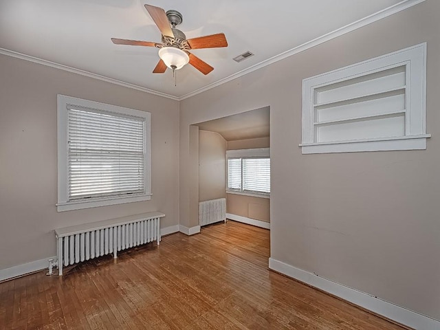 empty room featuring hardwood / wood-style flooring, ceiling fan, crown molding, and radiator heating unit