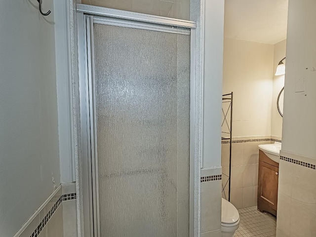 bathroom featuring toilet, tile patterned floors, vanity, tile walls, and a shower with shower door