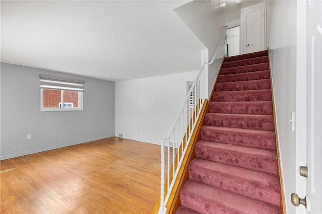 stairs with hardwood / wood-style floors and brick wall