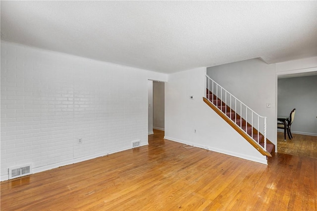 unfurnished living room with brick wall, a textured ceiling, and wood-type flooring