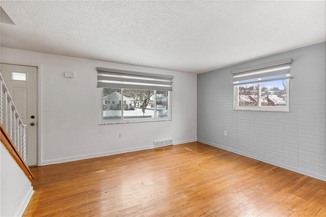 entryway with a textured ceiling, light hardwood / wood-style flooring, and brick wall