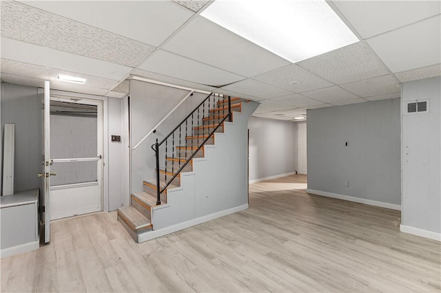 basement with a drop ceiling and light hardwood / wood-style flooring