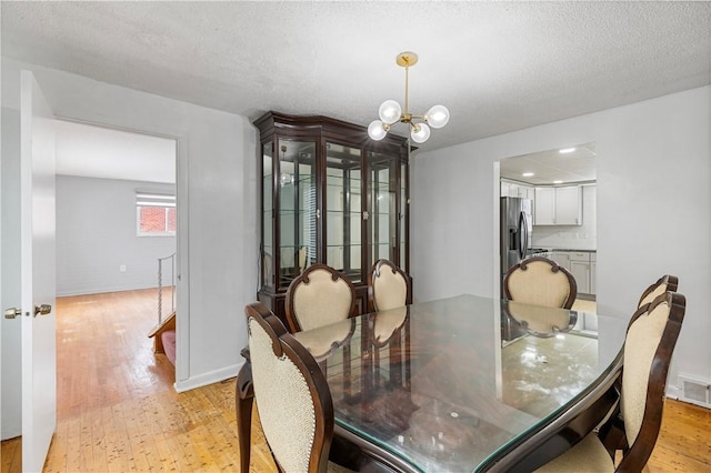 dining space featuring a textured ceiling, a chandelier, and light hardwood / wood-style flooring