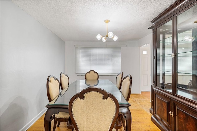 dining space featuring a notable chandelier, light wood-type flooring, and a textured ceiling