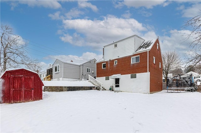 snow covered rear of property featuring a storage shed and a trampoline