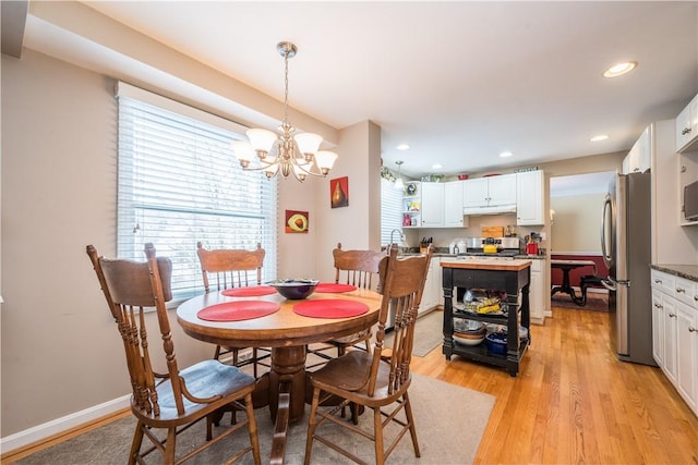 dining area featuring sink, light wood-type flooring, and an inviting chandelier