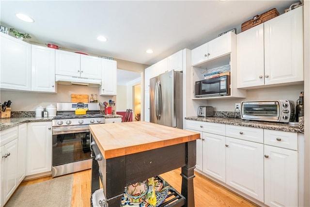 kitchen with stainless steel appliances, white cabinets, dark stone countertops, and light hardwood / wood-style floors