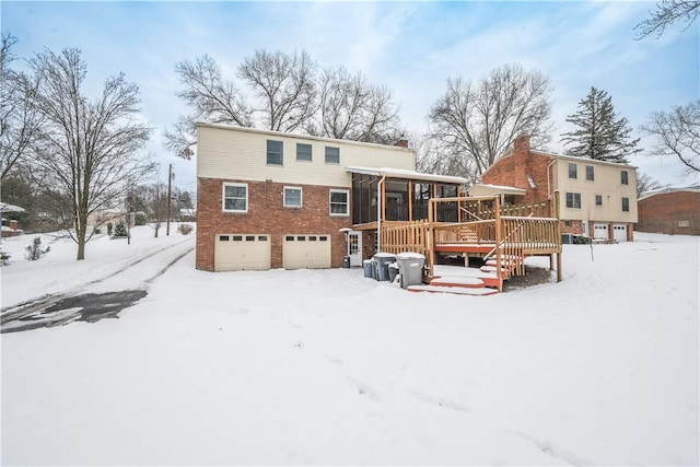 snow covered house featuring a sunroom, a garage, and a wooden deck