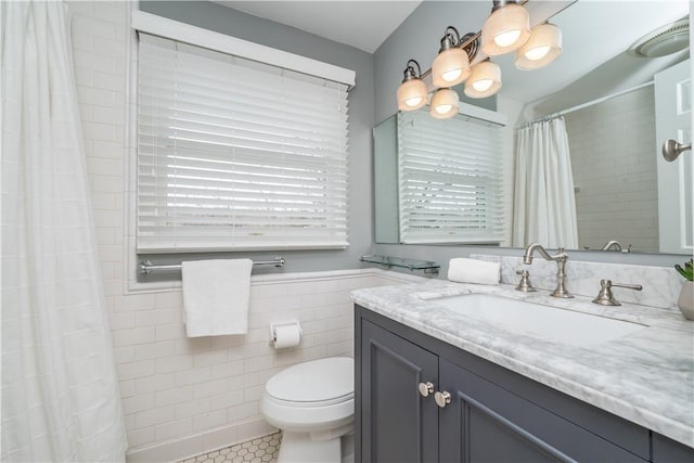 bathroom with toilet, curtained shower, tile patterned flooring, vanity, and tile walls