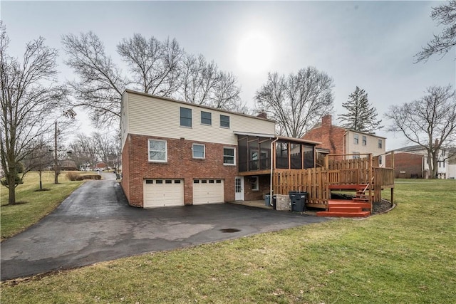 rear view of property with aphalt driveway, an attached garage, a sunroom, a lawn, and a chimney