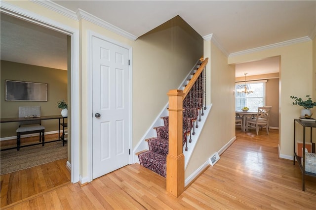 stairs featuring wood finished floors, visible vents, baseboards, ornamental molding, and an inviting chandelier