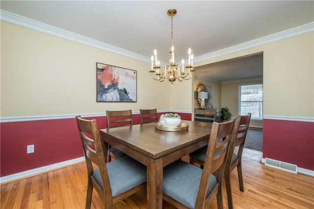 dining space featuring baseboards, visible vents, crown molding, and light wood finished floors