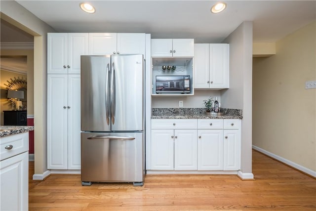 kitchen with light wood-style flooring, stone counters, freestanding refrigerator, and white cabinets