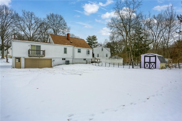 snow covered house with central AC and a storage shed