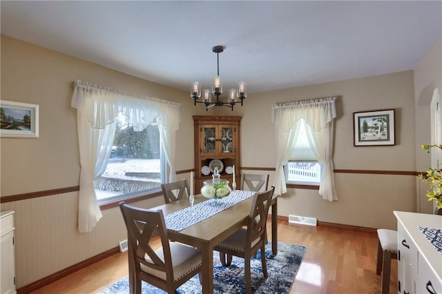 dining space with light wood-type flooring, an inviting chandelier, and wood walls