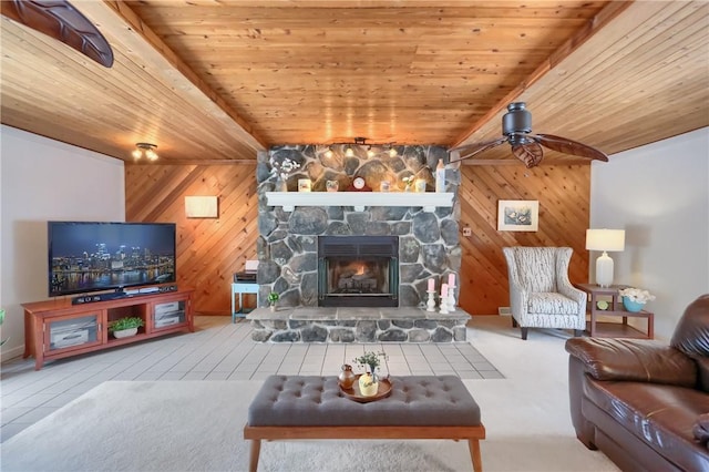 living room featuring wooden walls, beamed ceiling, ceiling fan, wood ceiling, and a stone fireplace