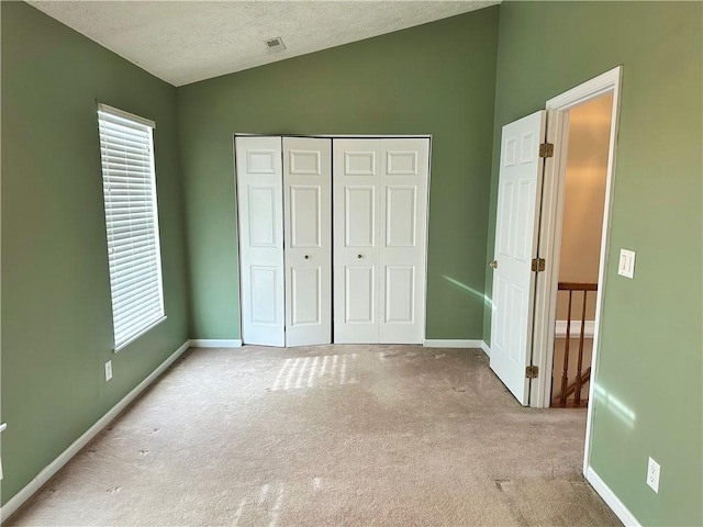 unfurnished bedroom with vaulted ceiling, light colored carpet, a closet, and a textured ceiling