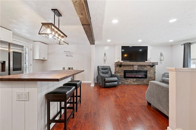 living room with dark hardwood / wood-style floors, beam ceiling, and a stone fireplace