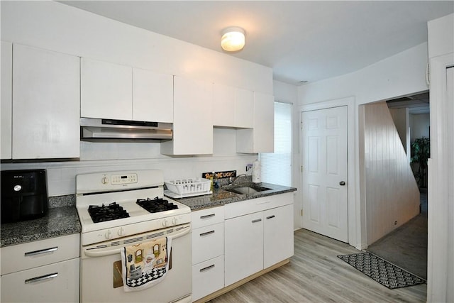 kitchen featuring light wood-type flooring, gas range gas stove, white cabinets, dark stone counters, and sink