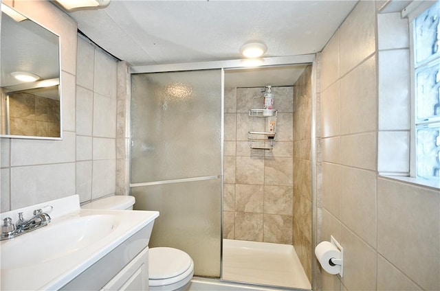 bathroom with tile walls, an enclosed shower, vanity, and toilet