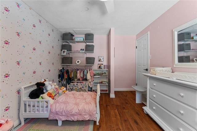 bedroom featuring a nursery area, a textured ceiling, ceiling fan, and dark hardwood / wood-style floors