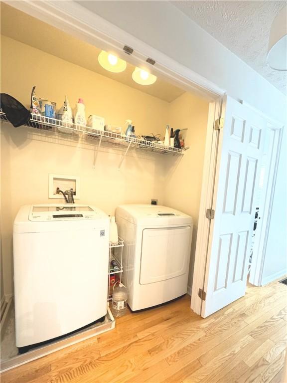 washroom with a textured ceiling, light hardwood / wood-style flooring, and separate washer and dryer