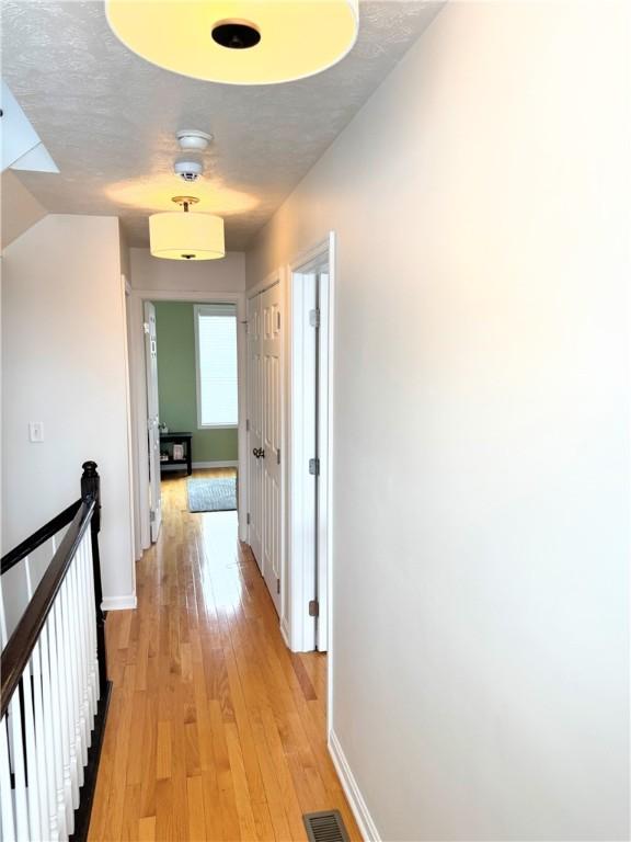 hall with a textured ceiling and light hardwood / wood-style flooring