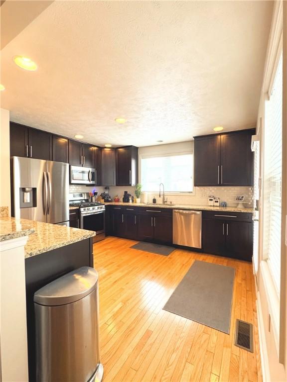 kitchen with stainless steel appliances, sink, light hardwood / wood-style floors, and light stone counters