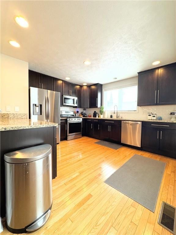 kitchen with stainless steel appliances, sink, light stone counters, light wood-type flooring, and dark brown cabinetry