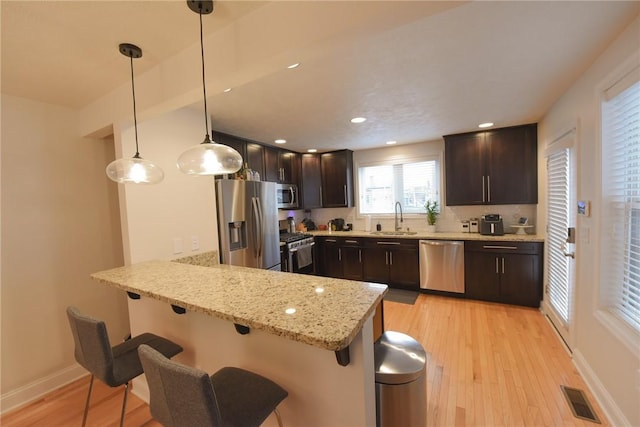 kitchen featuring decorative light fixtures, sink, a kitchen bar, kitchen peninsula, and stainless steel appliances