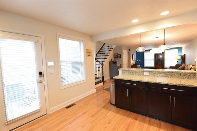 kitchen featuring dark brown cabinetry, pendant lighting, light stone counters, and light hardwood / wood-style floors