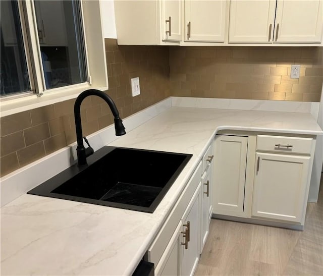 kitchen with sink, light stone counters, light hardwood / wood-style flooring, decorative backsplash, and white cabinets