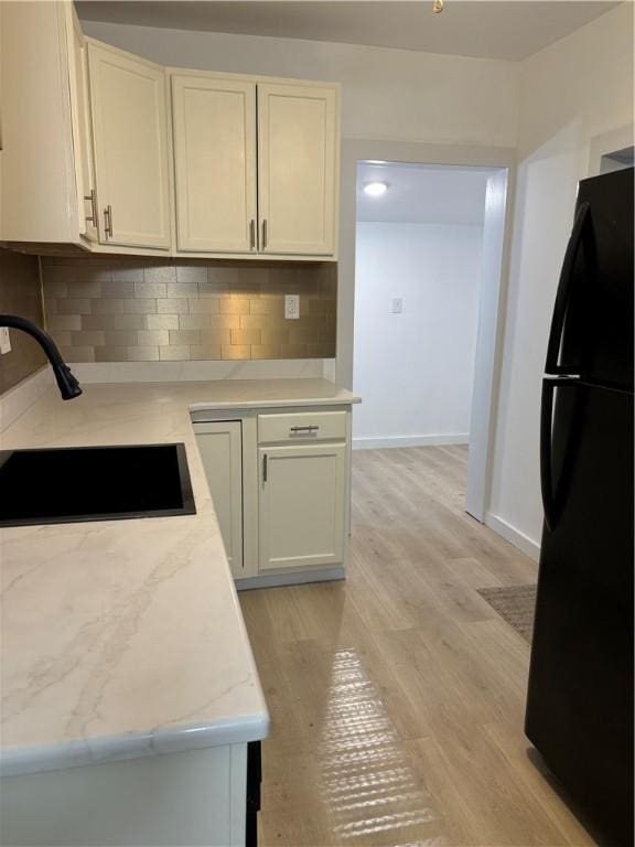 kitchen with sink, black refrigerator, light stone countertops, light hardwood / wood-style floors, and decorative backsplash