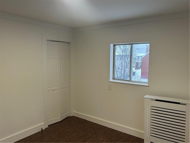 unfurnished bedroom with dark wood-type flooring, heating unit, and a closet