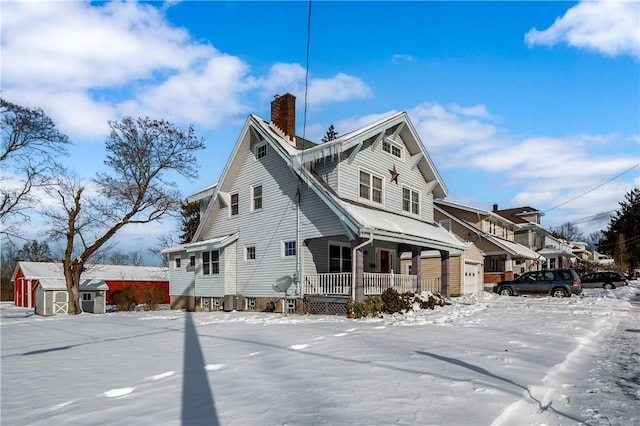 snow covered property featuring a porch and a storage unit