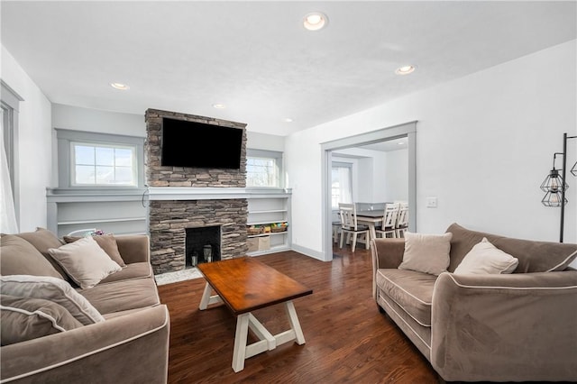 living room featuring dark hardwood / wood-style flooring, a healthy amount of sunlight, and a stone fireplace